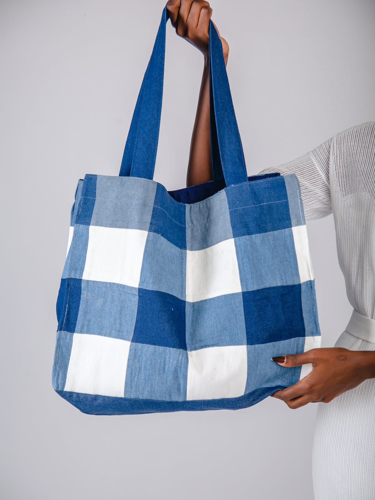 Blue and white checkered tote bag held by a person against a gray background