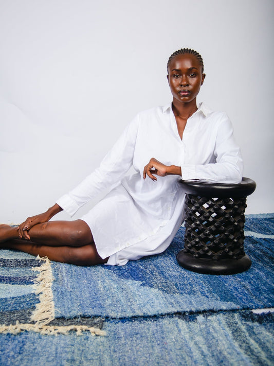Woman in a white shirt sitting on a blue rug with a black stool.