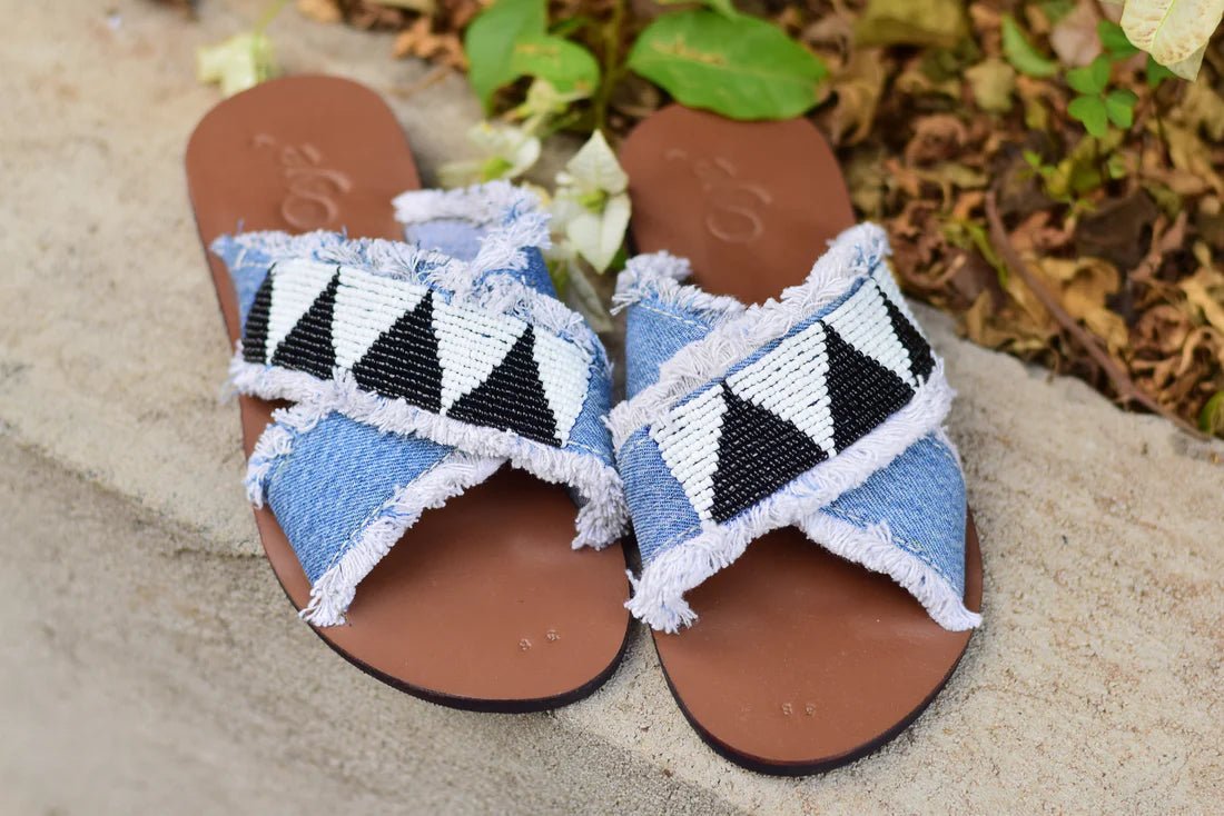 Pair of sandals with blue and black patterned straps on a natural stone surface.