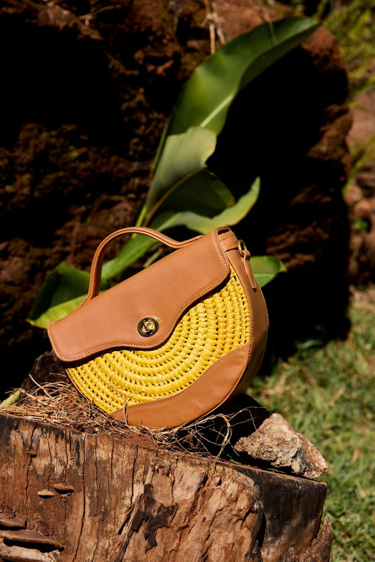 Yellow woven handbag with brown leather accents on a wooden log