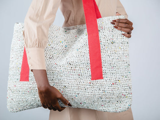 Person holding a textured tote bag with a red strap against a neutral background
