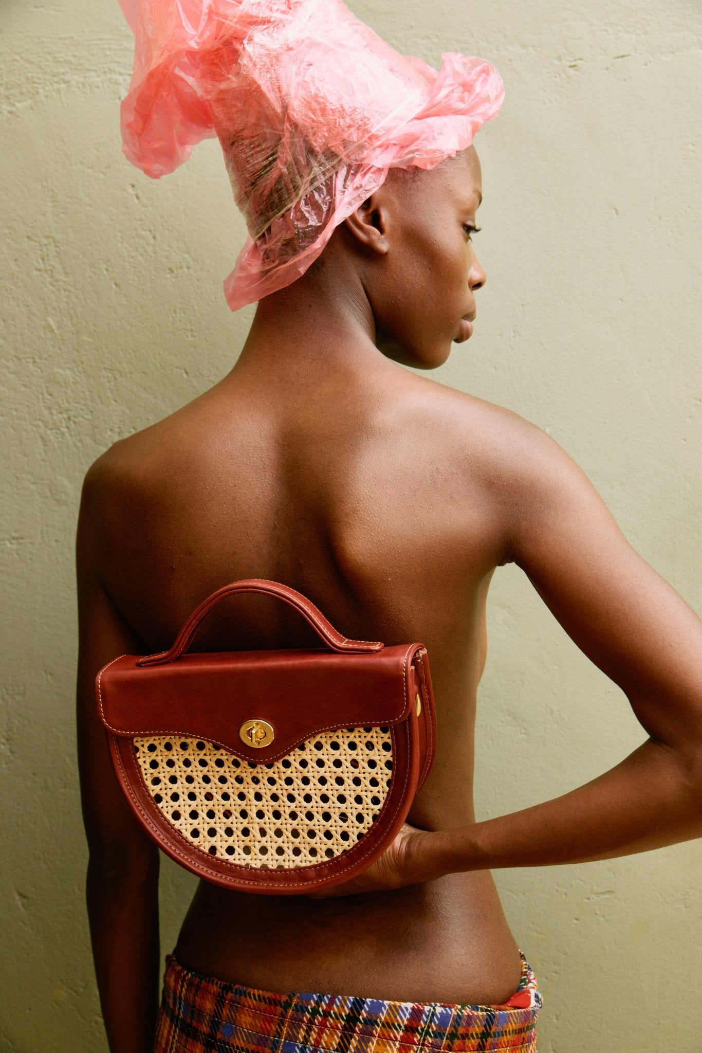 Woman wearing a pink shower cap holding a red handbag with a yellow logo against a plain background