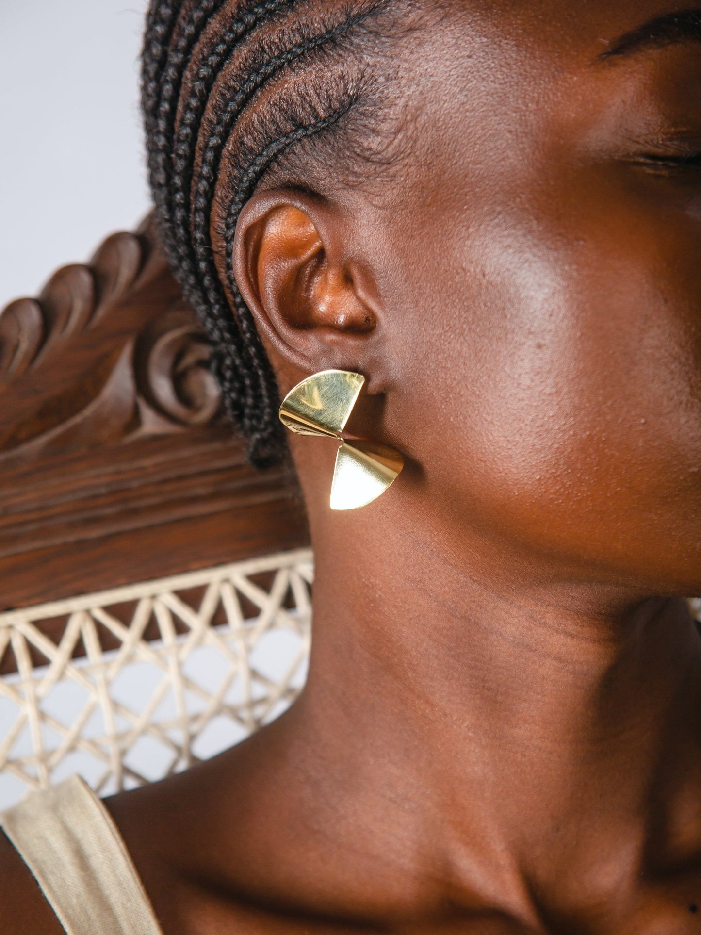 Gold triangular earring worn by a person with braided hair.