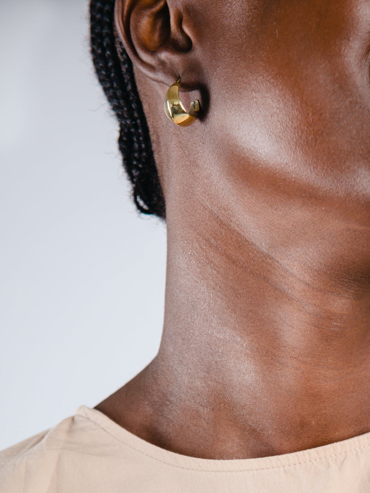 Close-up of a person wearing gold hoop earrings with a neutral background