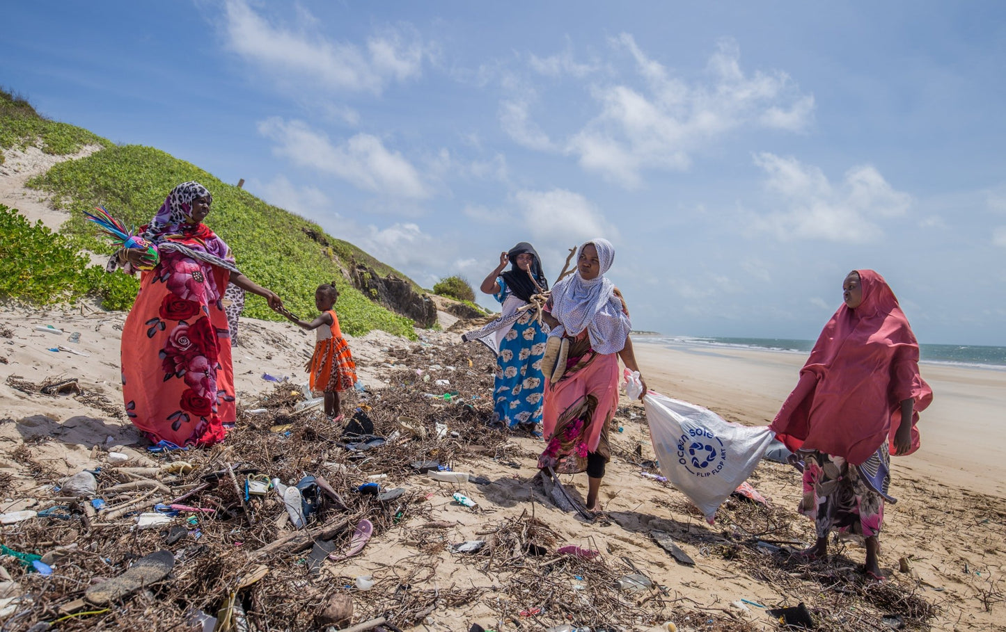 Group of people cleaning up trash on a beach with a visible environmental organization logo.