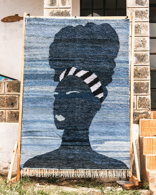 Textile art piece with a silhouette design on a wooden stand against a stone wall.