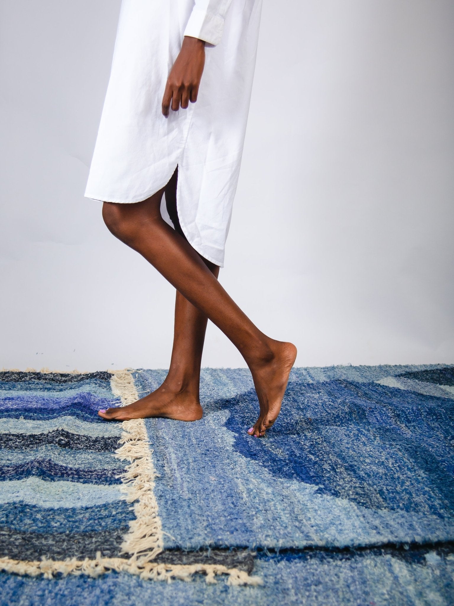 Person wearing a white dress standing on a blue textured rug.