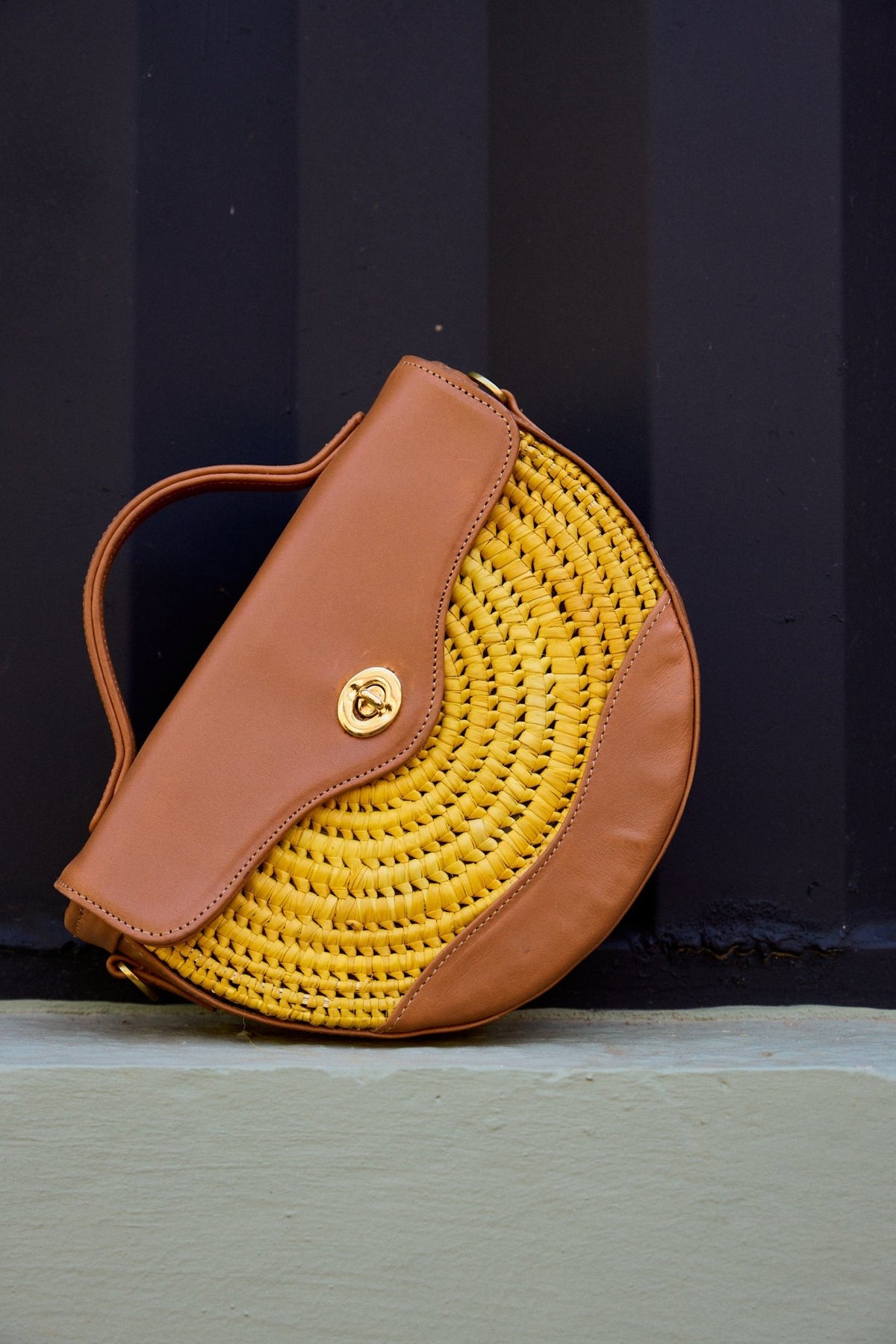 Yellow woven handbag with brown leather strap on a dark background