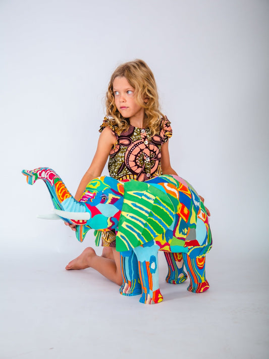 Child sitting on a colourful elephant sculpture against a white background