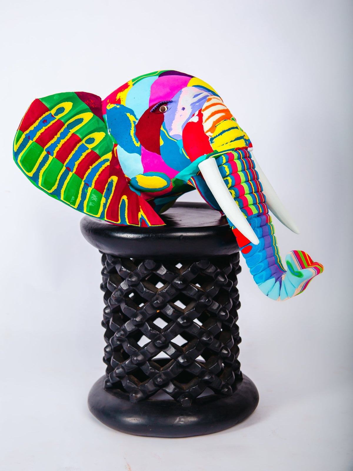 Colourful elephant sculpture on a black wooden stool against a white background