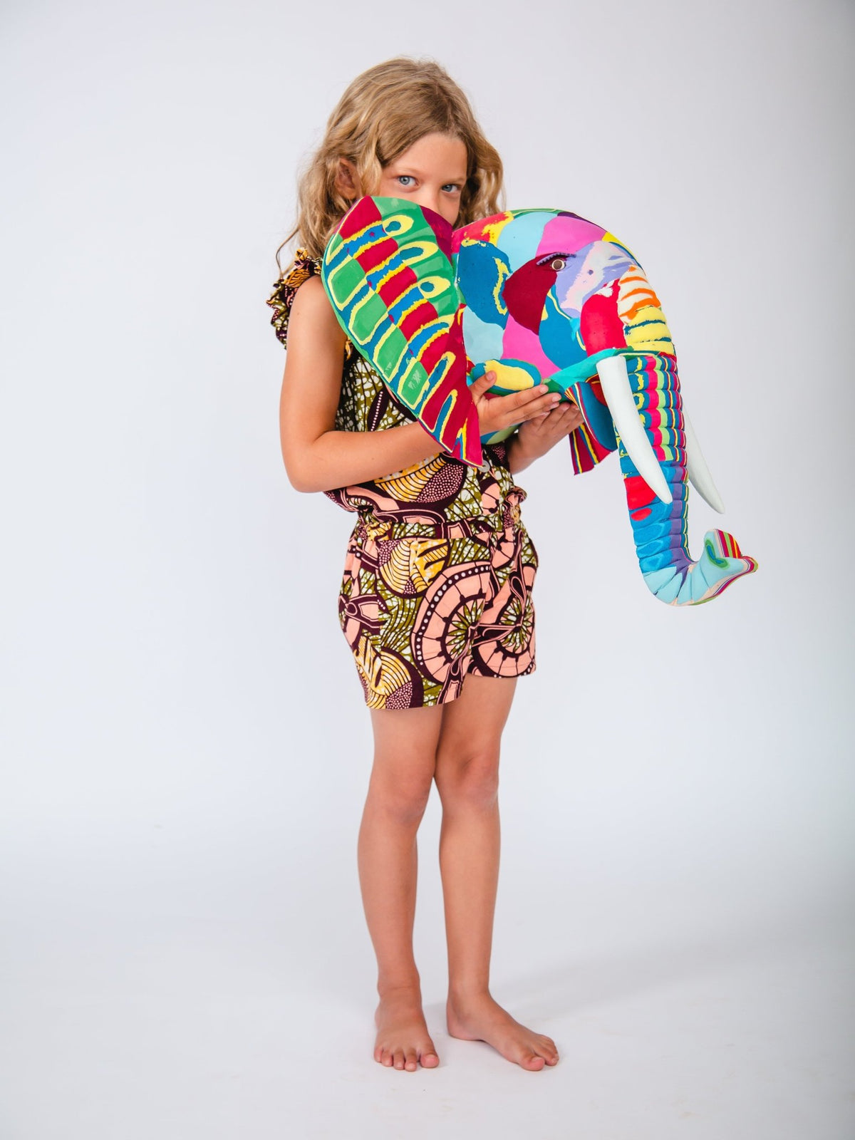 Child holding a colourful elephant-shaped sculpture against a white background