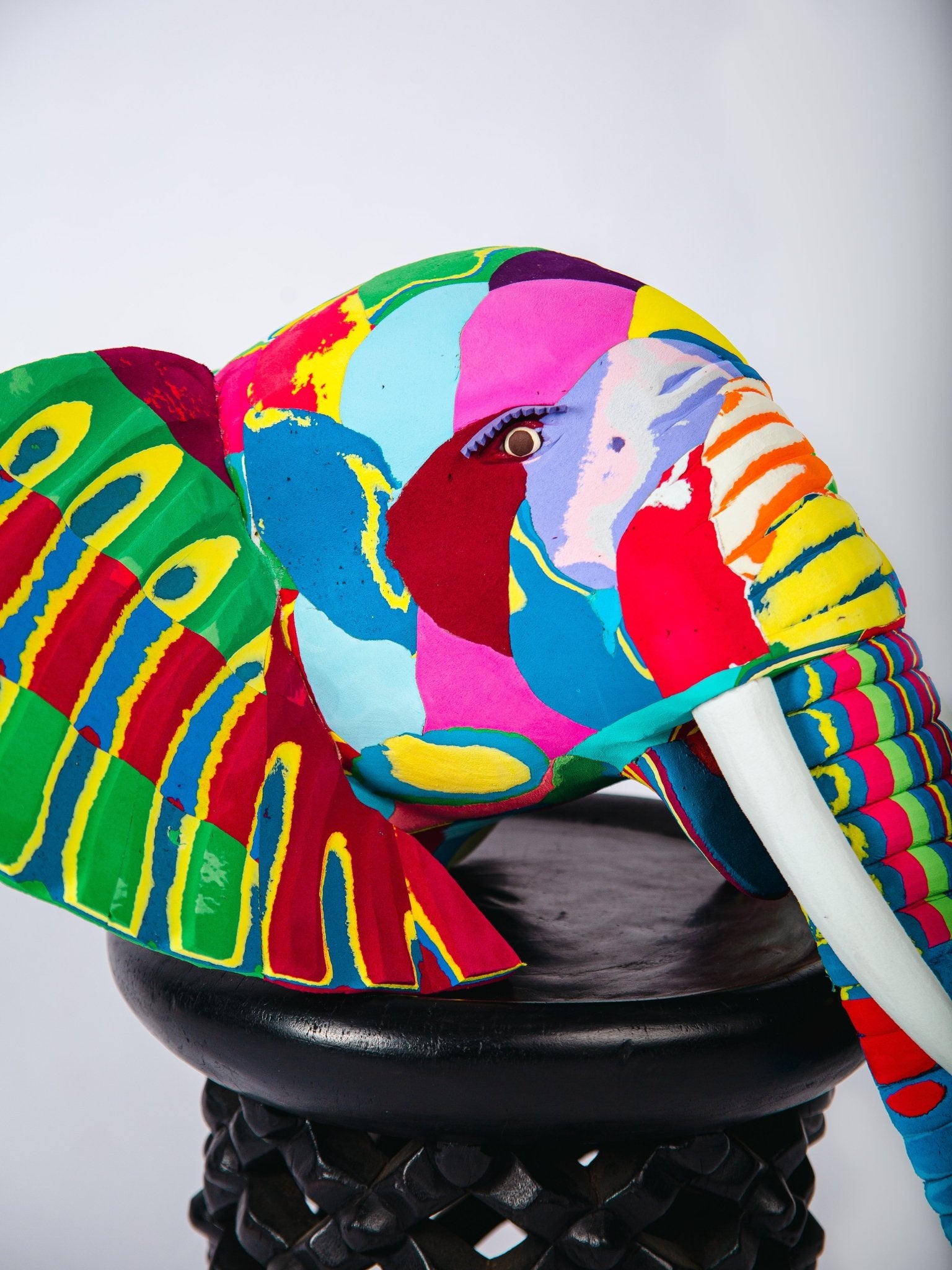 Colourful elephant-shaped object on a black stand against a white background