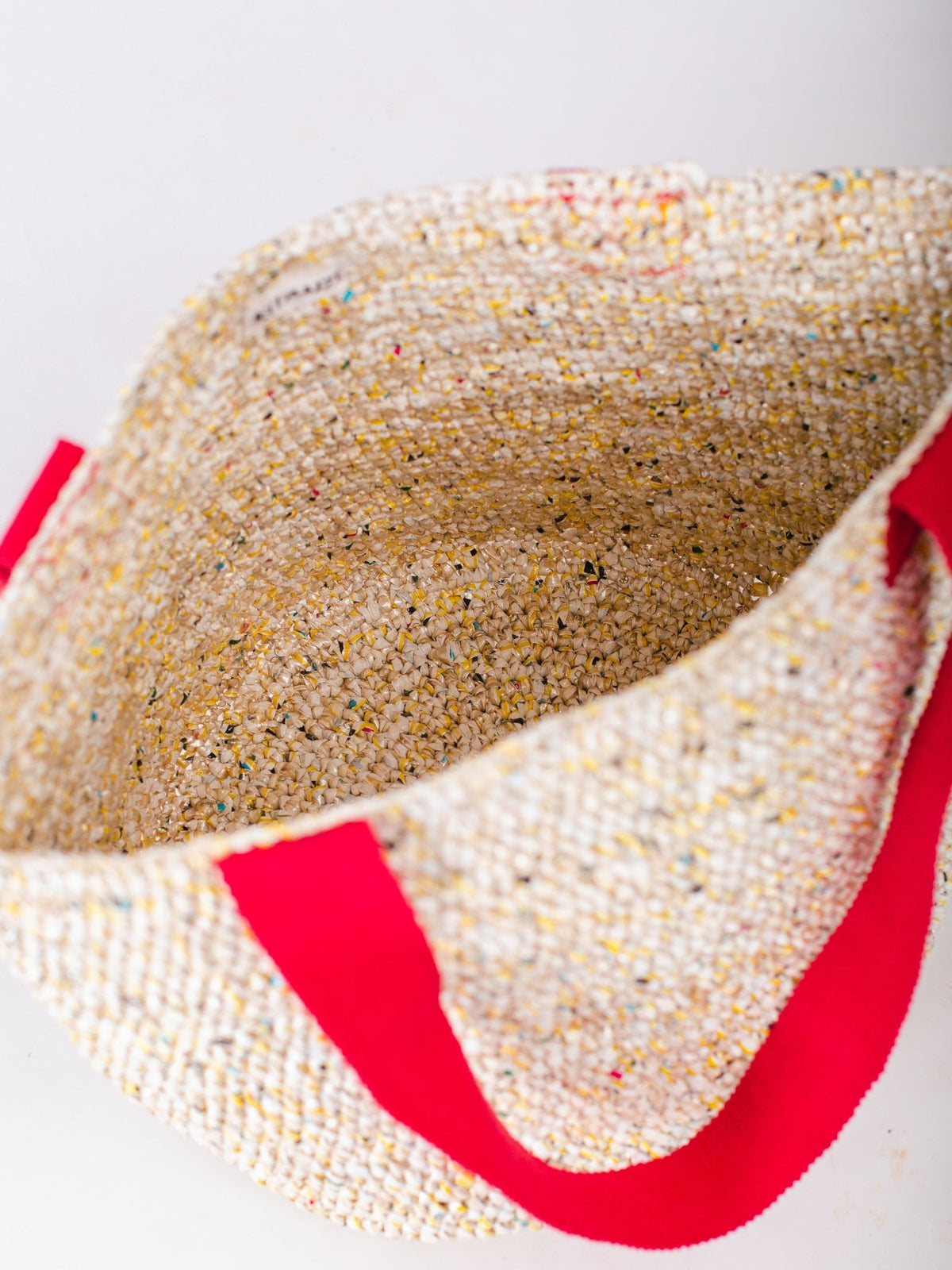 Close-up of a textured beige bag with red handles on a white background