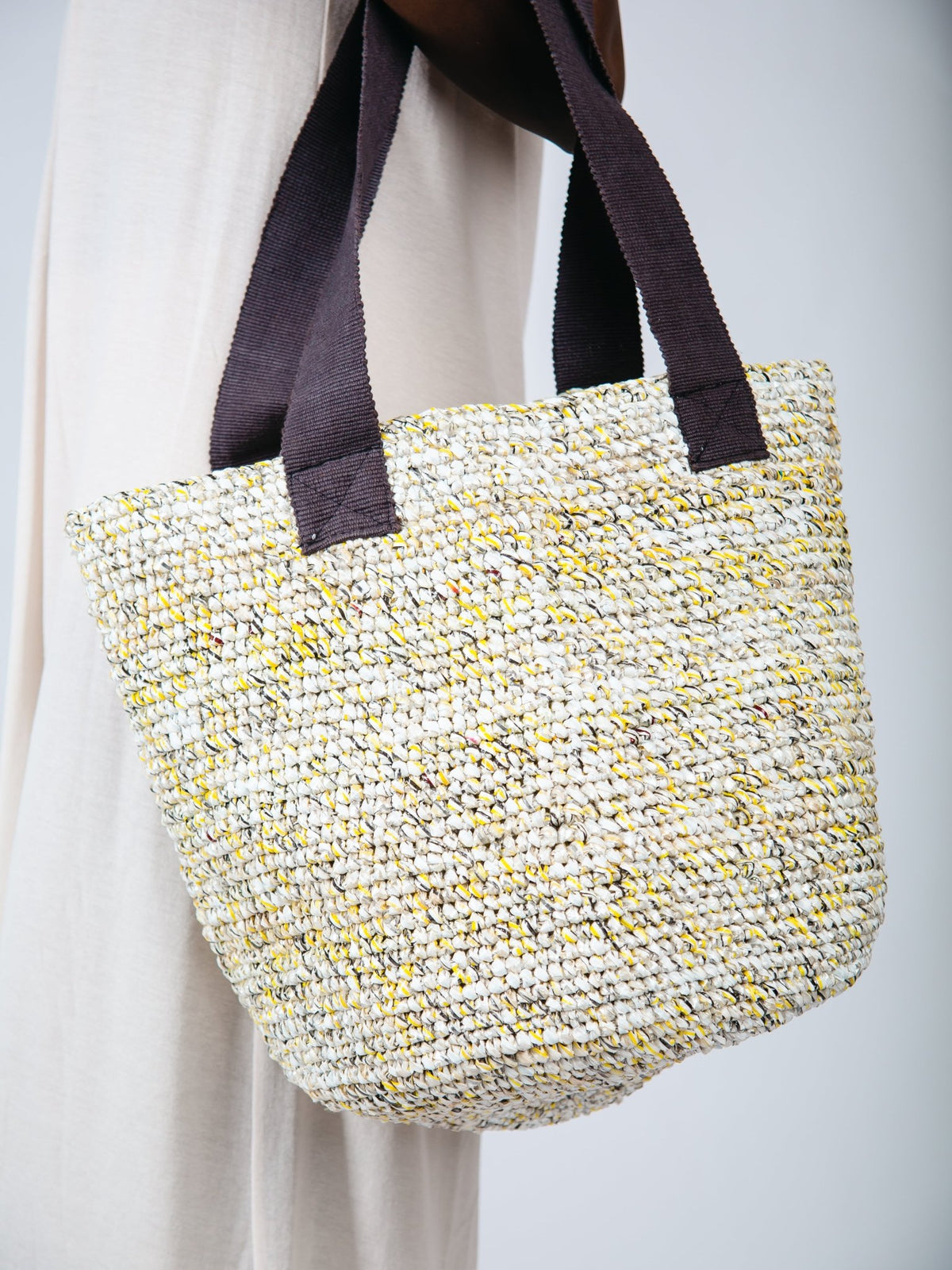 Woven handbag with brown straps on a plain background