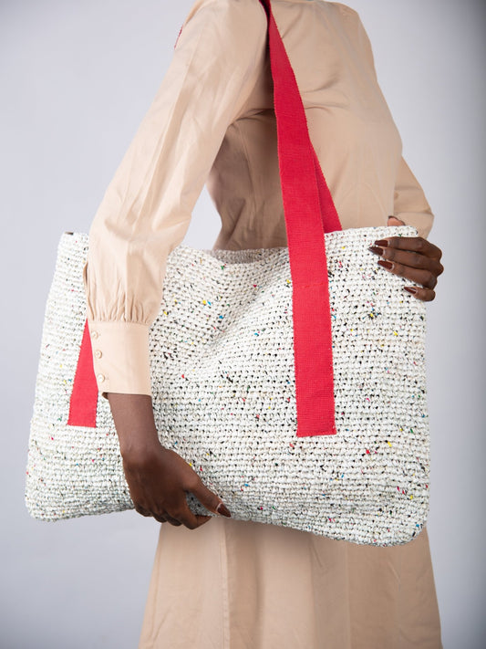Person holding a woven bag with red straps against a plain background