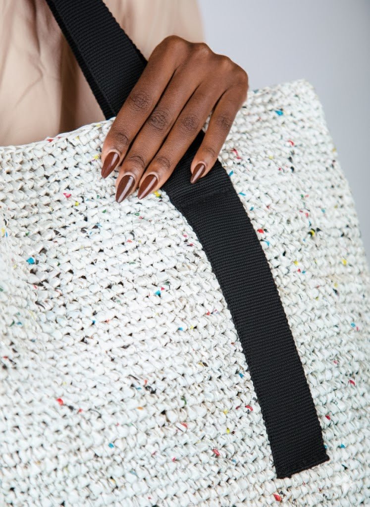 Hand holding a textured white bag with a black strap against a neutral background