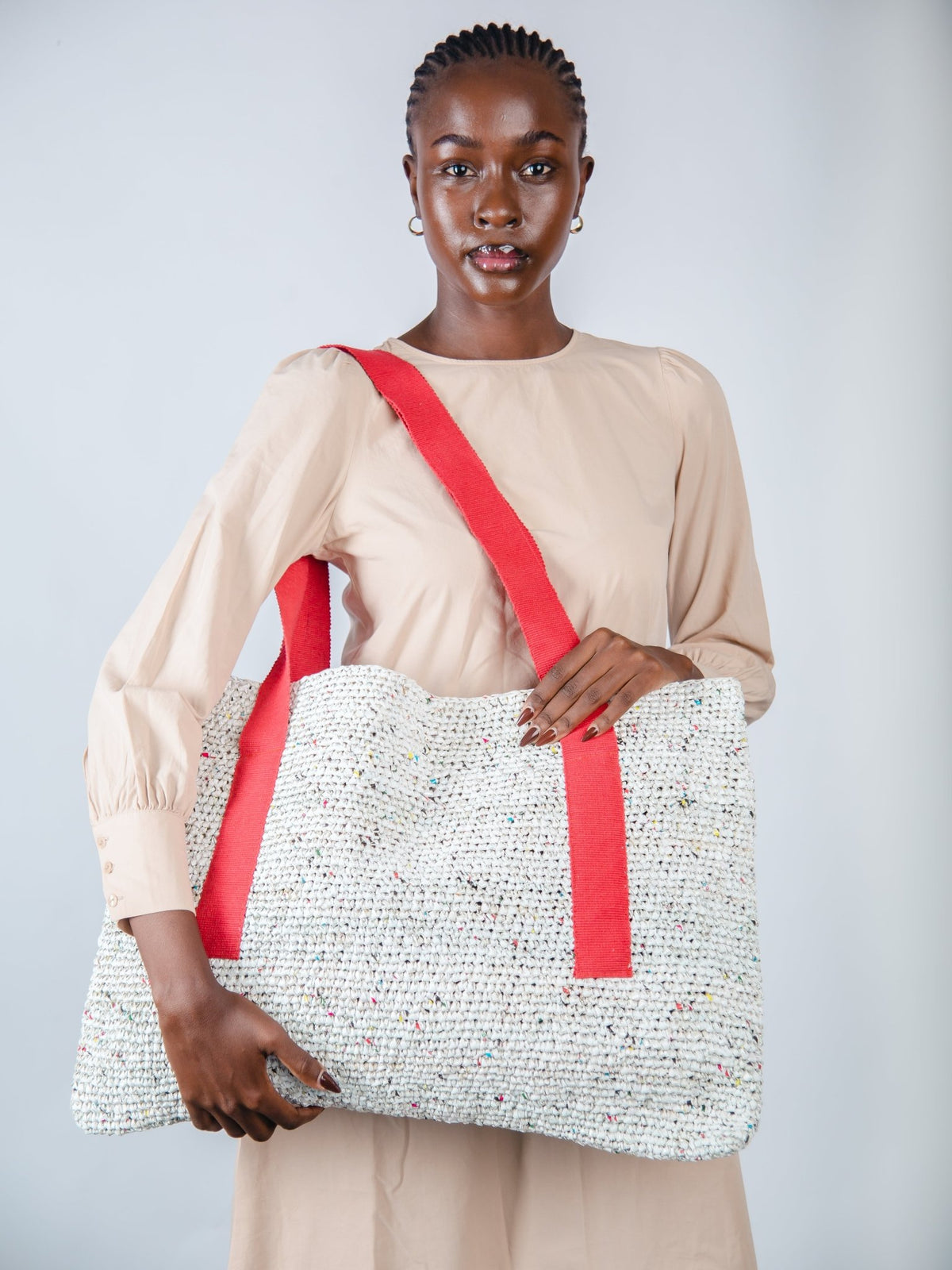 Woman holding a textured white bag with a red strap against a plain background