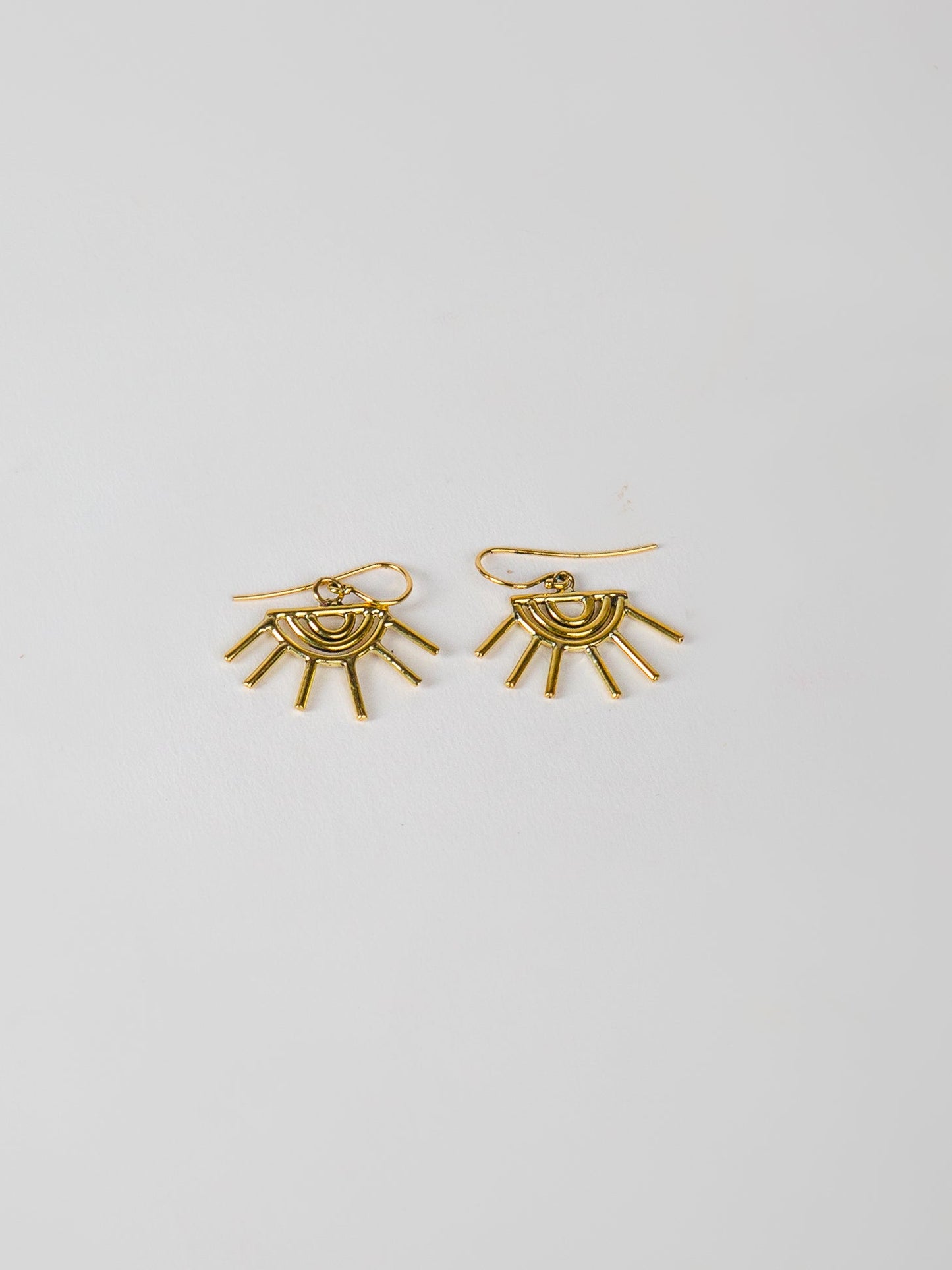 Gold sun-shaped earrings on a light gray background