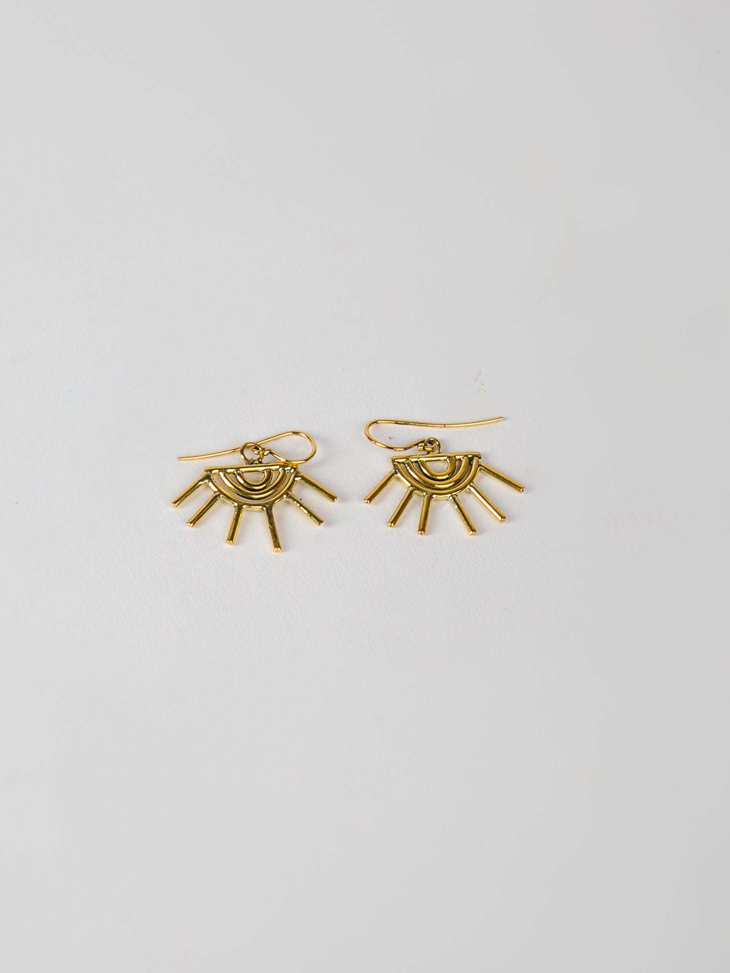 Gold sun-shaped earrings on a light gray background