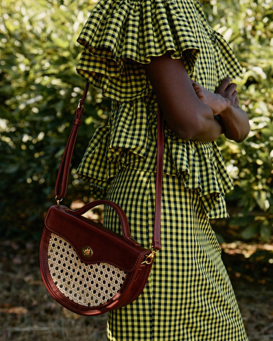 Person wearing a green and yellow checkered dress holding a red handbag with a textured pattern.