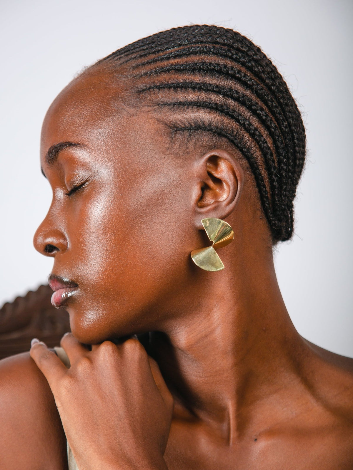 Woman with braided hair wearing gold earrings against a neutral background