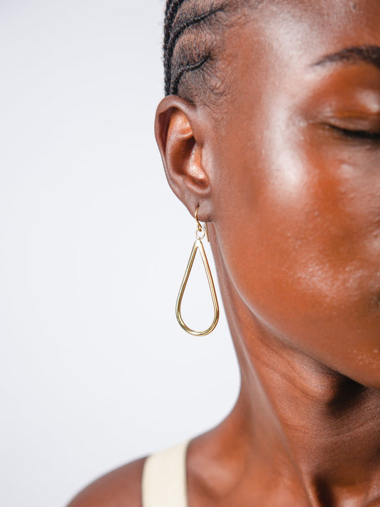 Close-up of a person wearing a gold teardrop earring against a white background