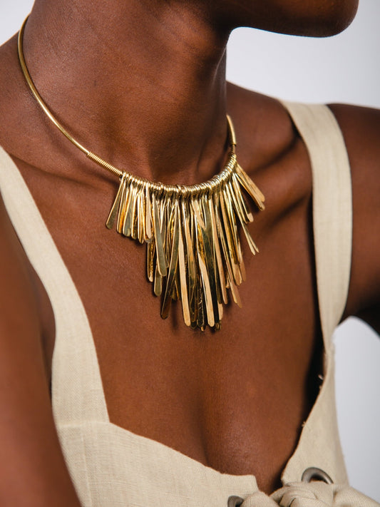 Gold fringe necklace worn by a person against a neutral background