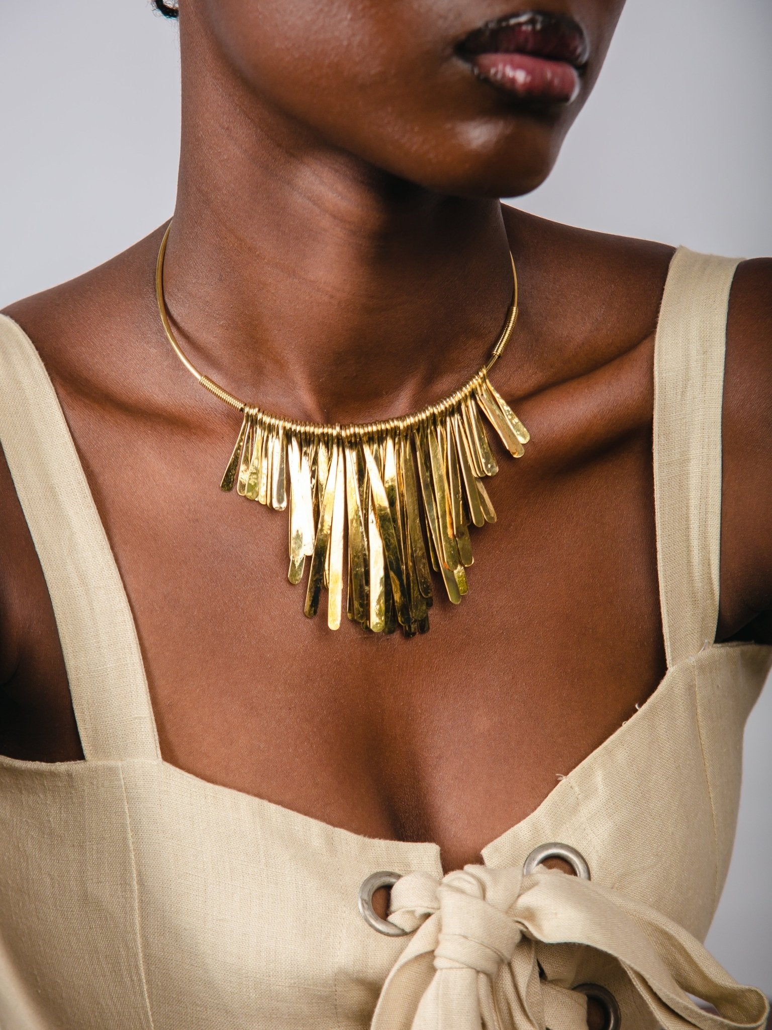 Woman wearing a gold fringe necklace with a beige top against a neutral background