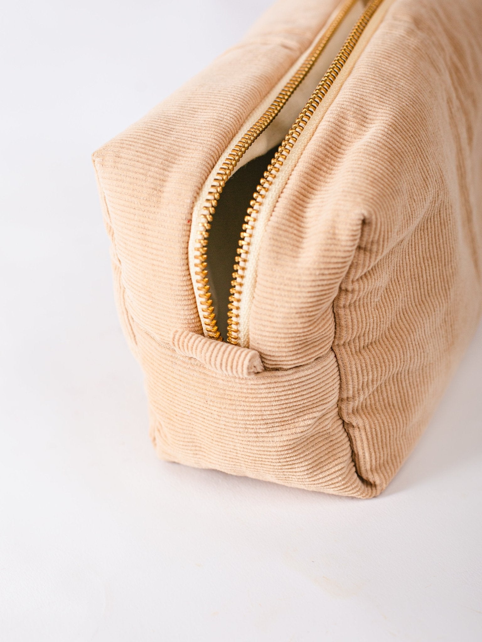 Beige corduroy pouch with a gold zipper on a white background