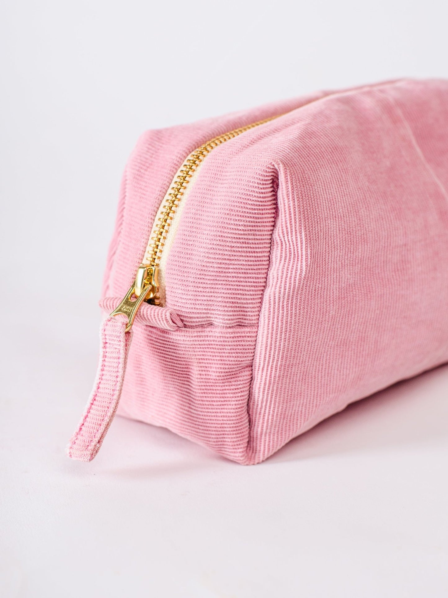 Pink velvet pouch with gold zipper on a light gray background