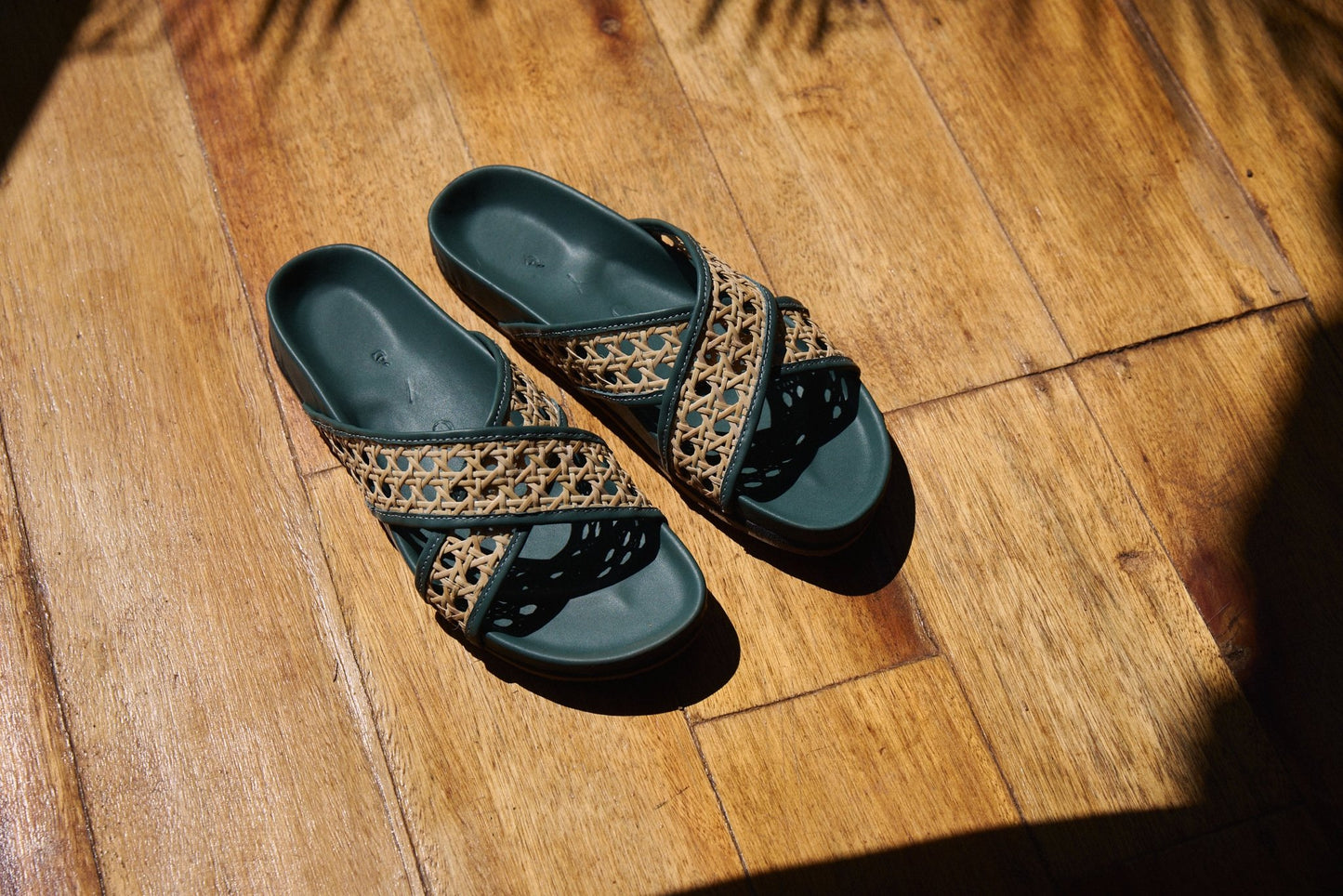 Pair of green sandals with decorative straps on a wooden floor