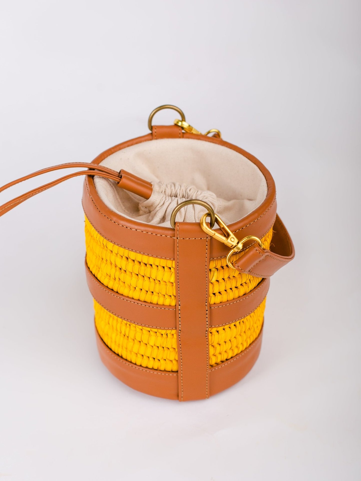 Yellow woven bucket bag with brown leather accents on a white background