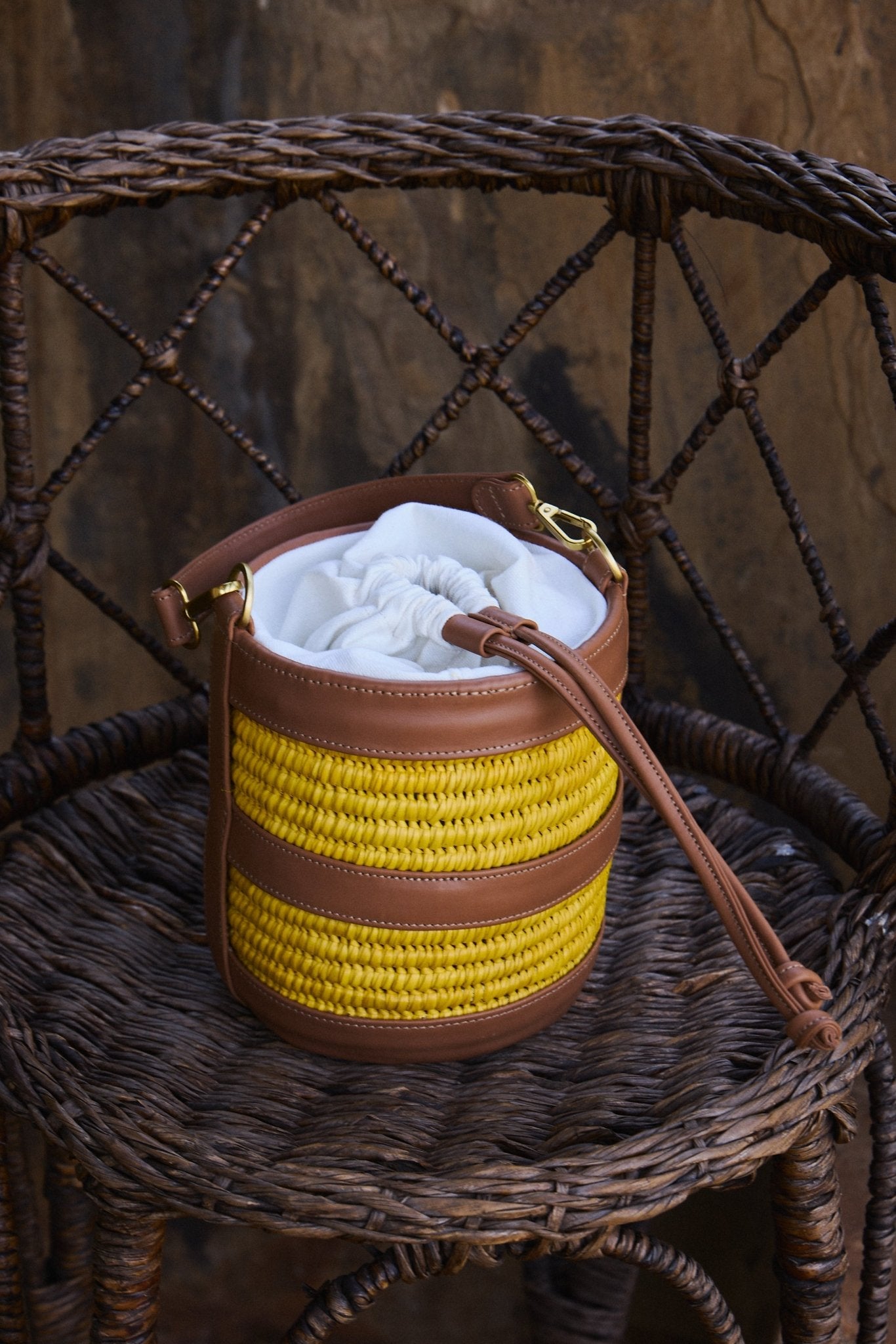 Small handbag with yellow woven bottom and brown top on a wicker chair