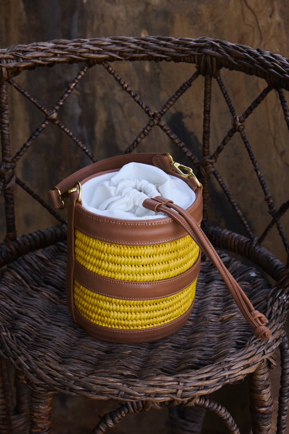 Small handbag with yellow woven bottom and brown top on a wicker chair