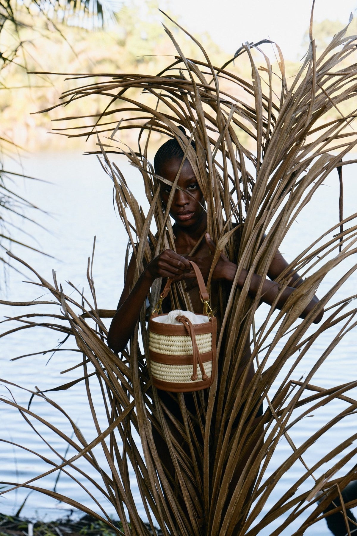 Person holding a woven basket amidst tall grasses by a body of water