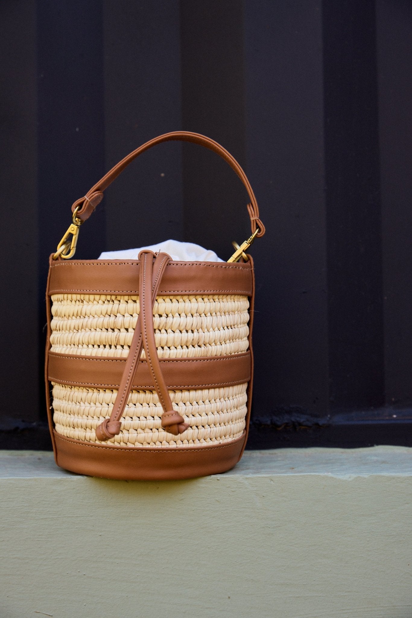 Woven handbag with brown leather accents on a dark background