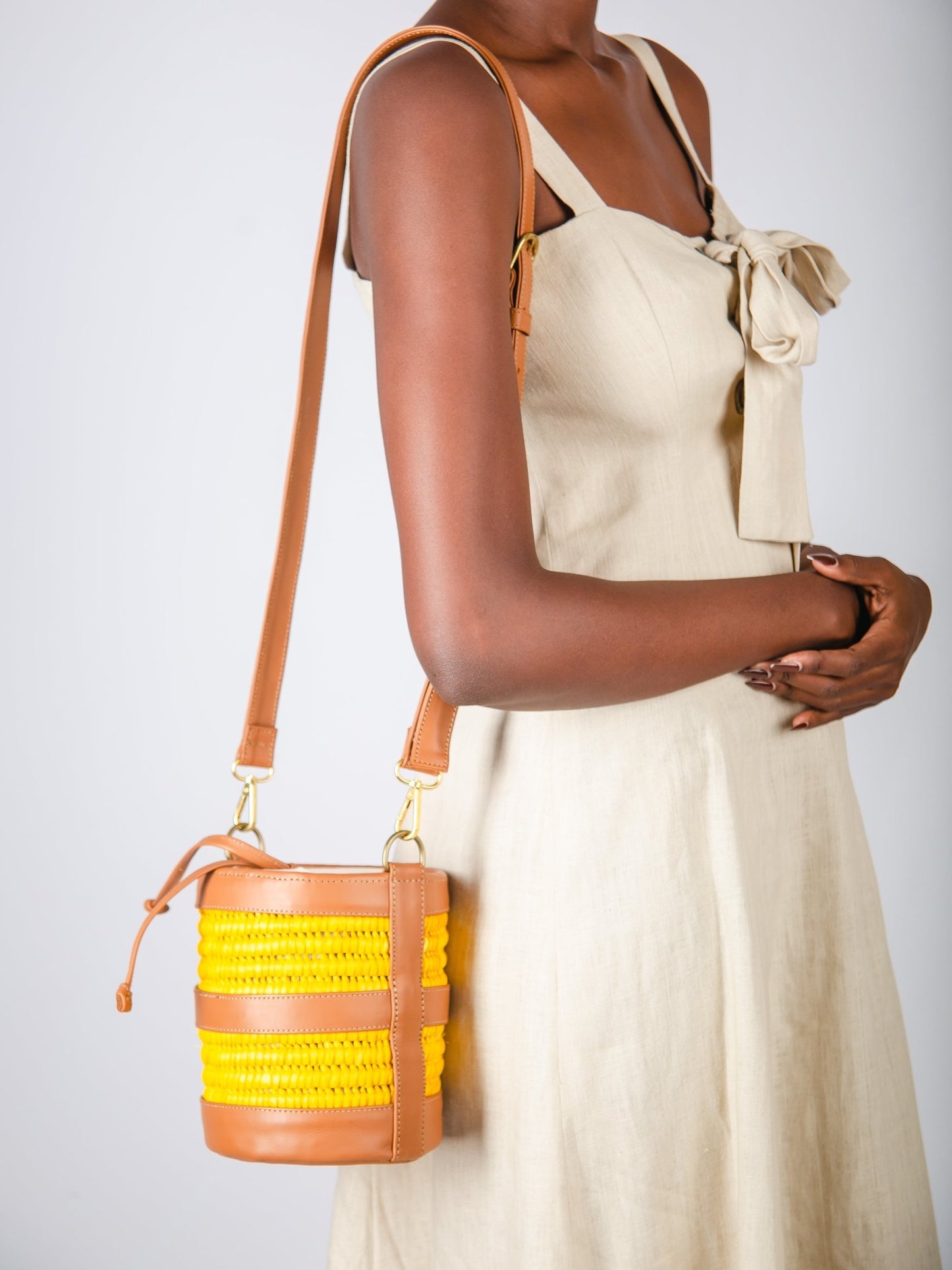 Woman holding a brown handbag with yellow accents against a plain background