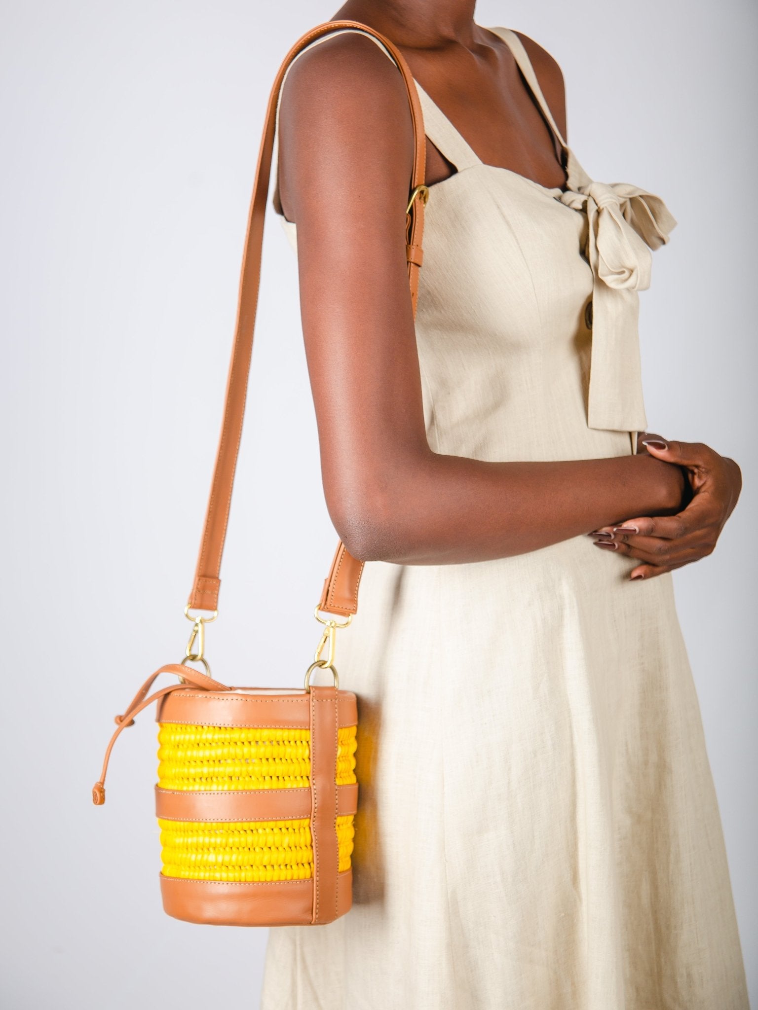 Woman holding a brown handbag with yellow accents against a plain background