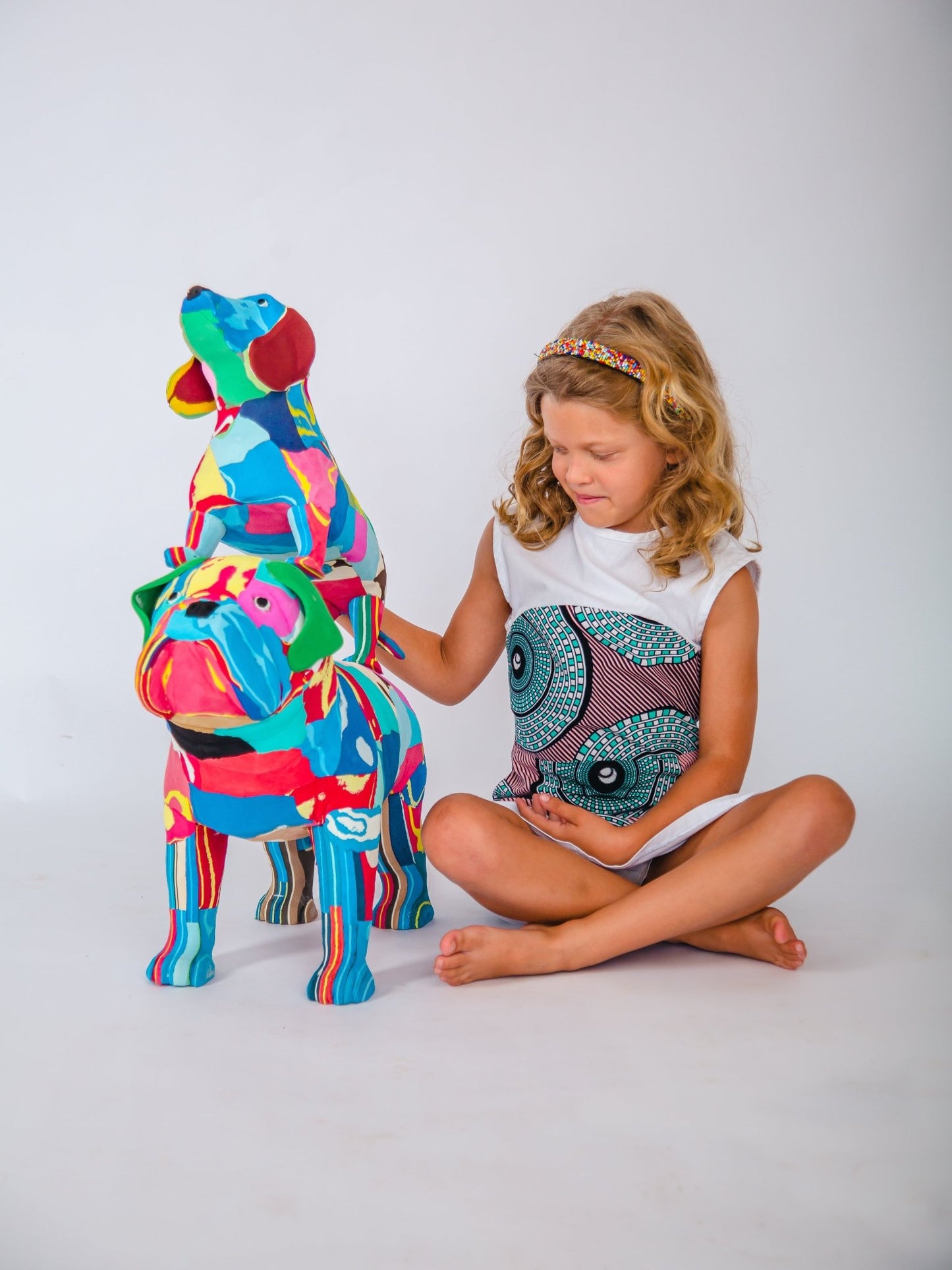 Child sat with a colourful dog-shaped sculpture on a white background