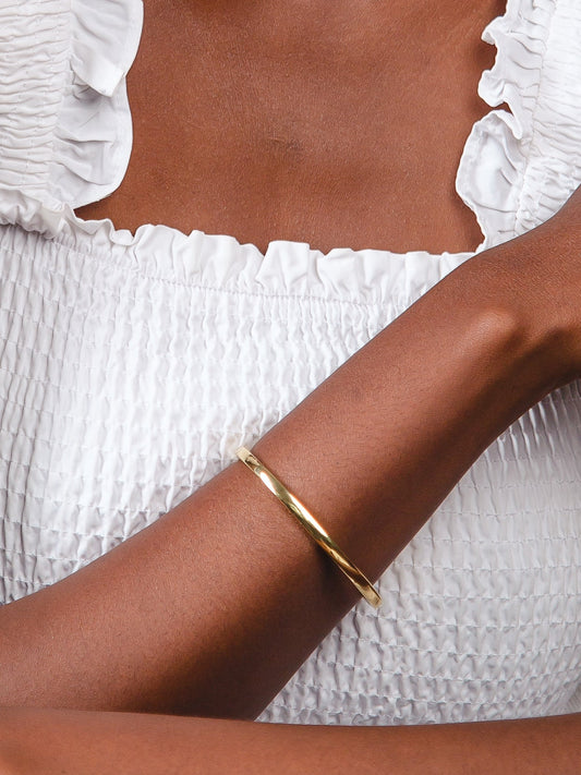 Gold bracelet on a wrist with a white textured garment in the background