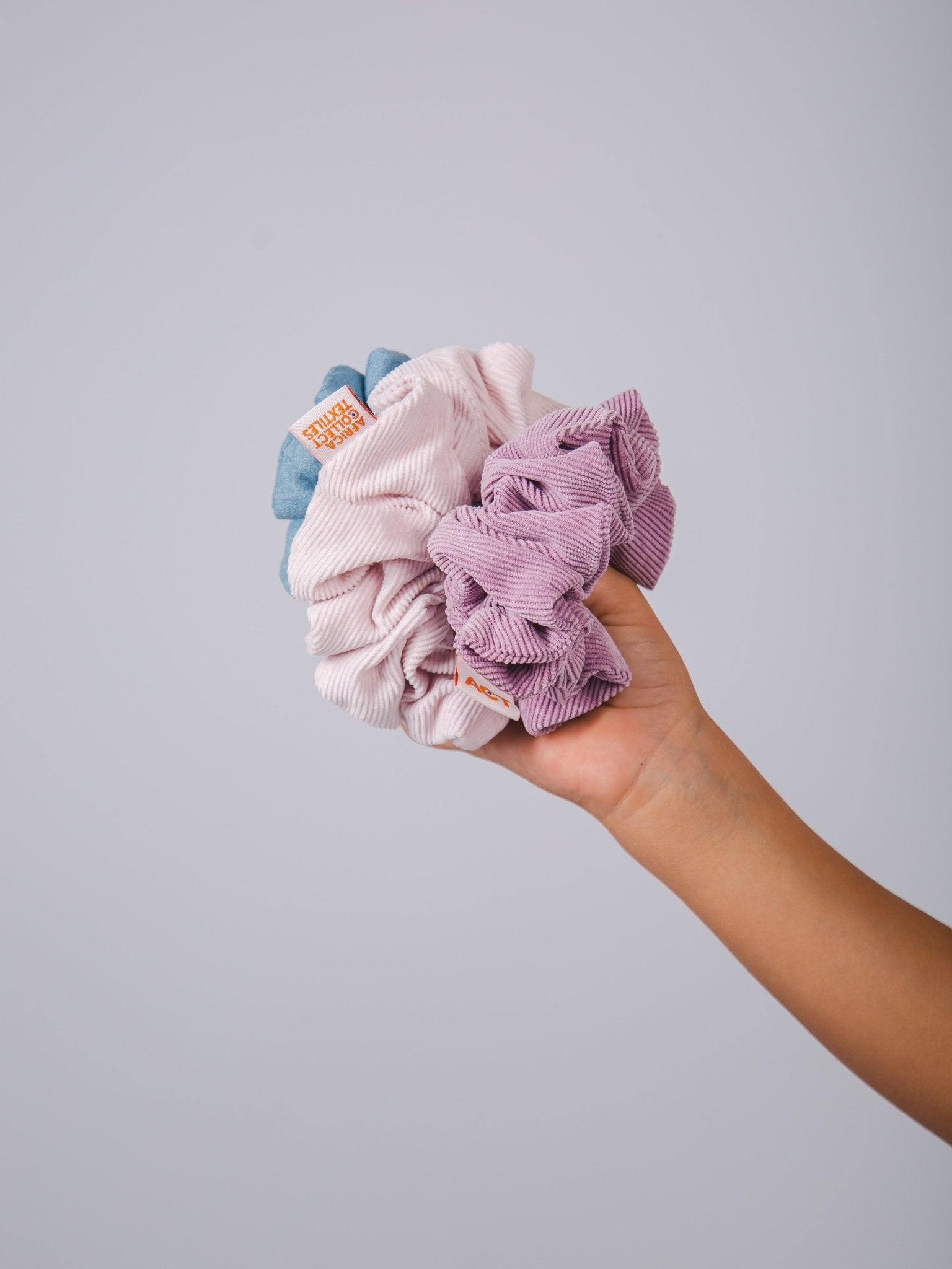 Hand holding three scrunchies against a gray background