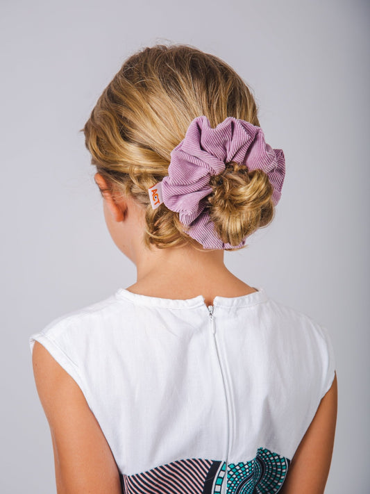 Woman with a stylish hair bun decorated with a purple scrunchie on a plain background