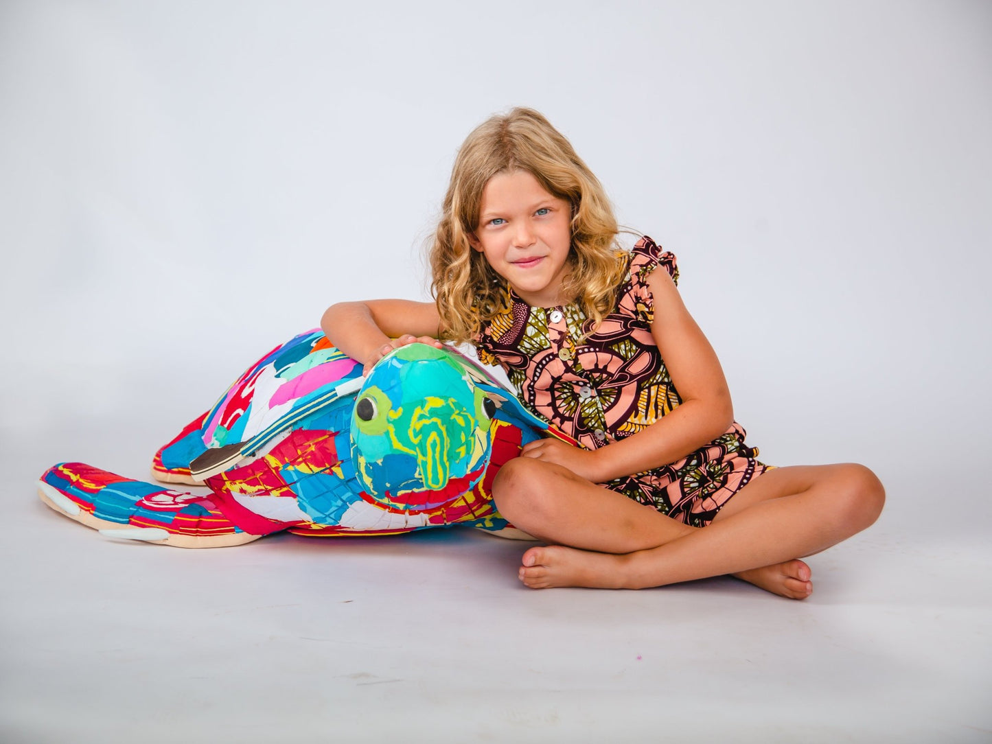 Young girl sitting next to a colourful turtle sculpture on a white background