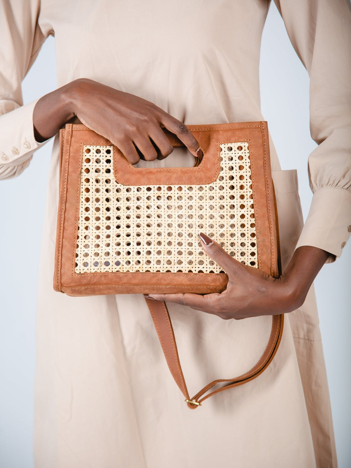 Person holding a brown handbag with a woven pattern against a neutral background