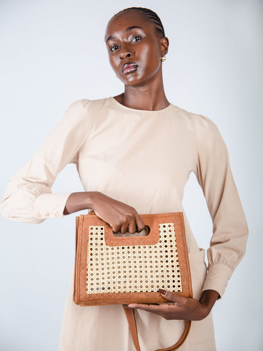 Woman holding a woven handbag against a plain background