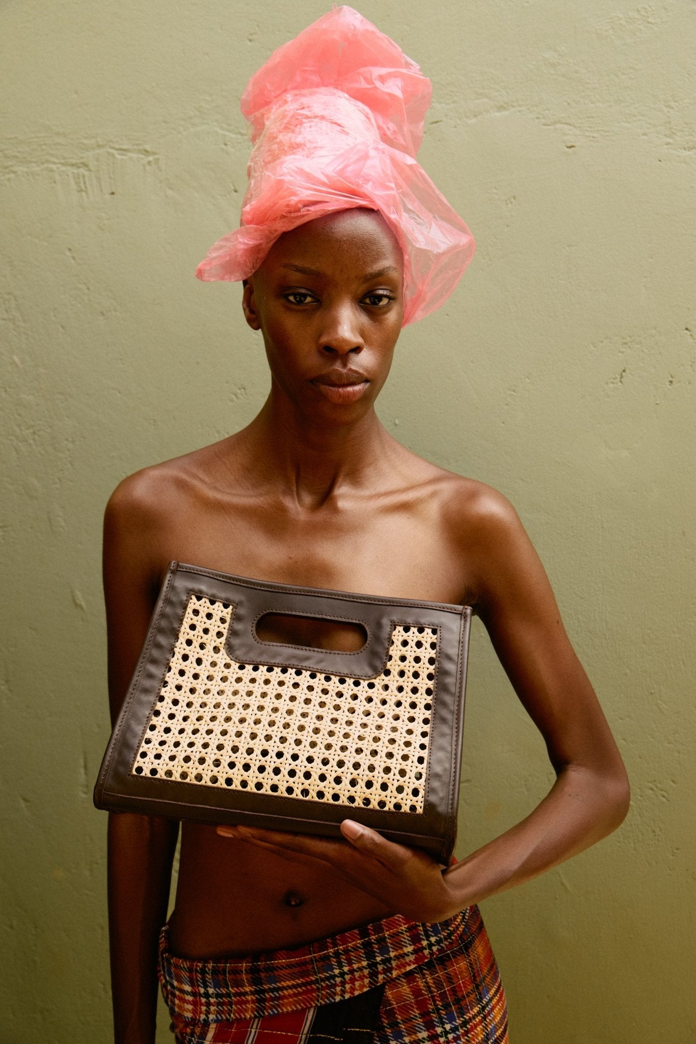 Woman holding a woven basket with a pink headscarf on a green background