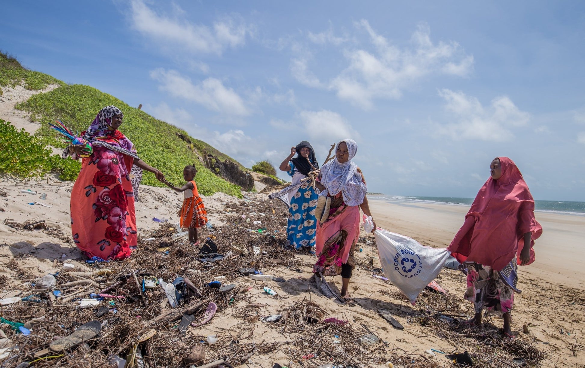 Group of people cleaning up trash on a beach with a visible environmental organization logo.